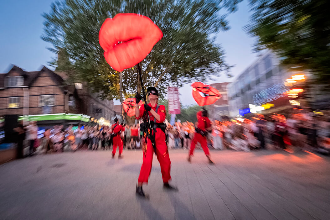 Three giant lips puppets in front of a crowd. The photo is blurred as if by motion.