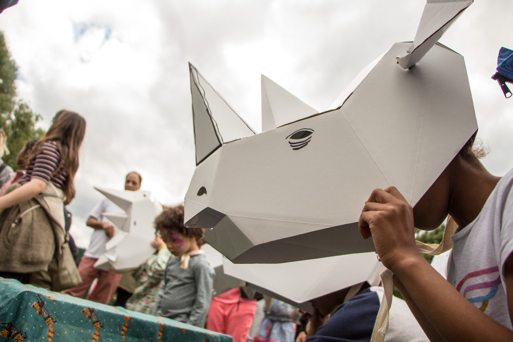 A person in a 3D card rhino mask. Behind them are other people, some holding masks.