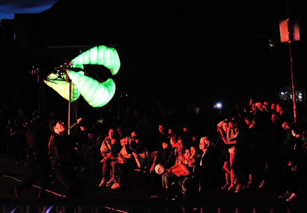 Two large lips puppets lit up green in front of a crowd at night.