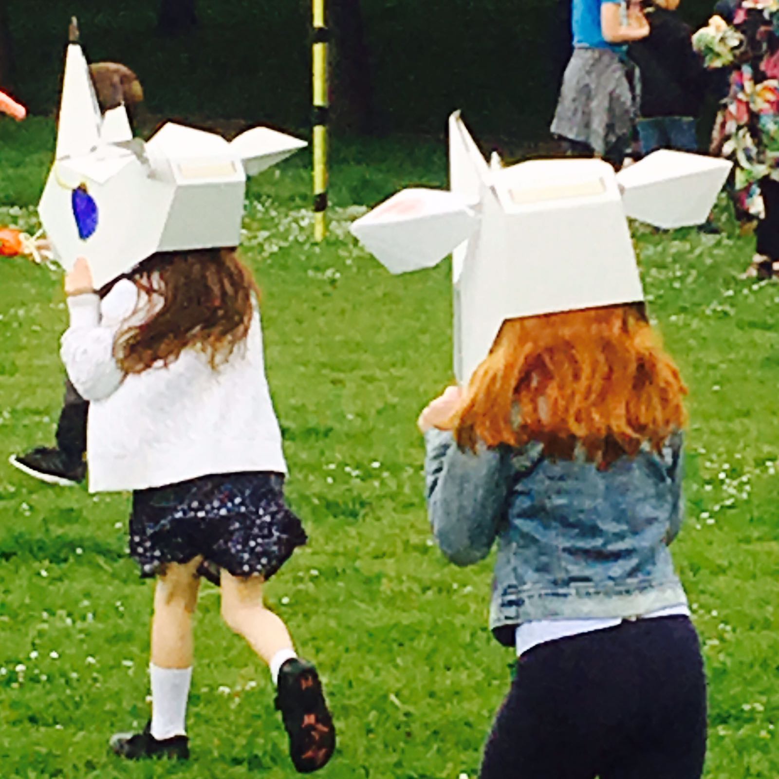 Two children, facing away from the camera, wearing white 3D rhino masks which they have decorated.