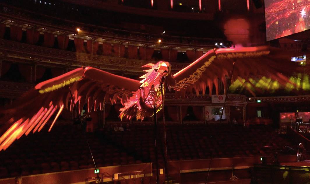 A large puppet of a red bird, 'flying' in an empty auditorium.