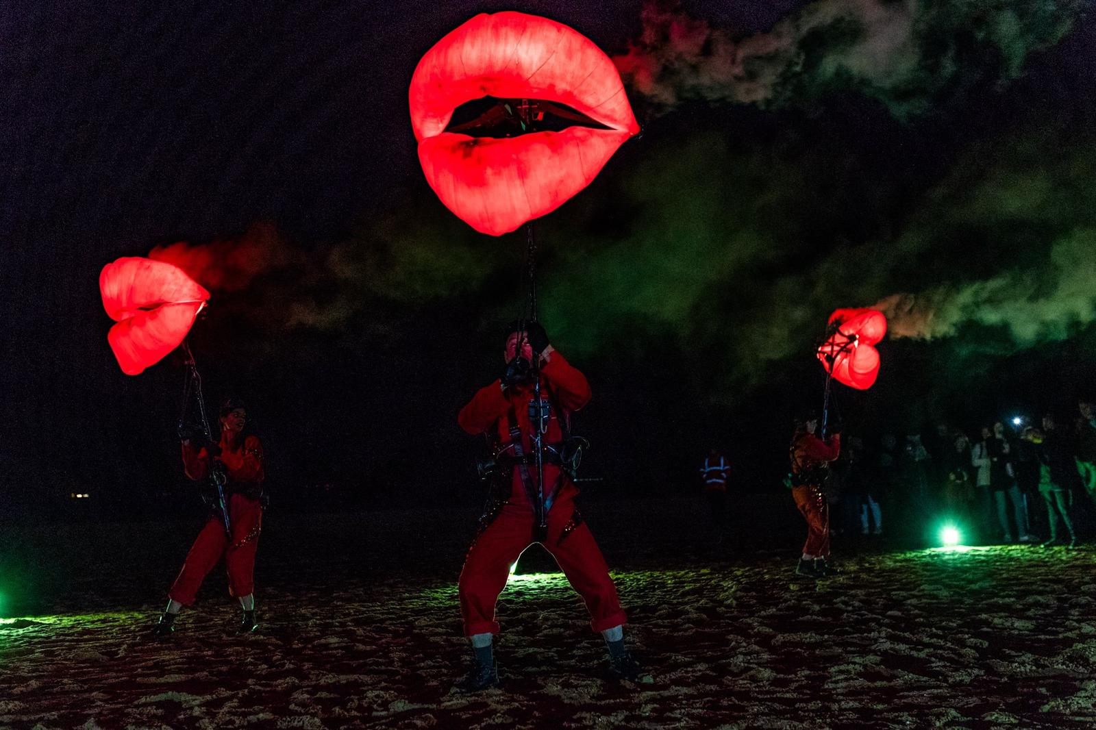 Three giant puppets shaped like pairs of lips glow red in the dark.