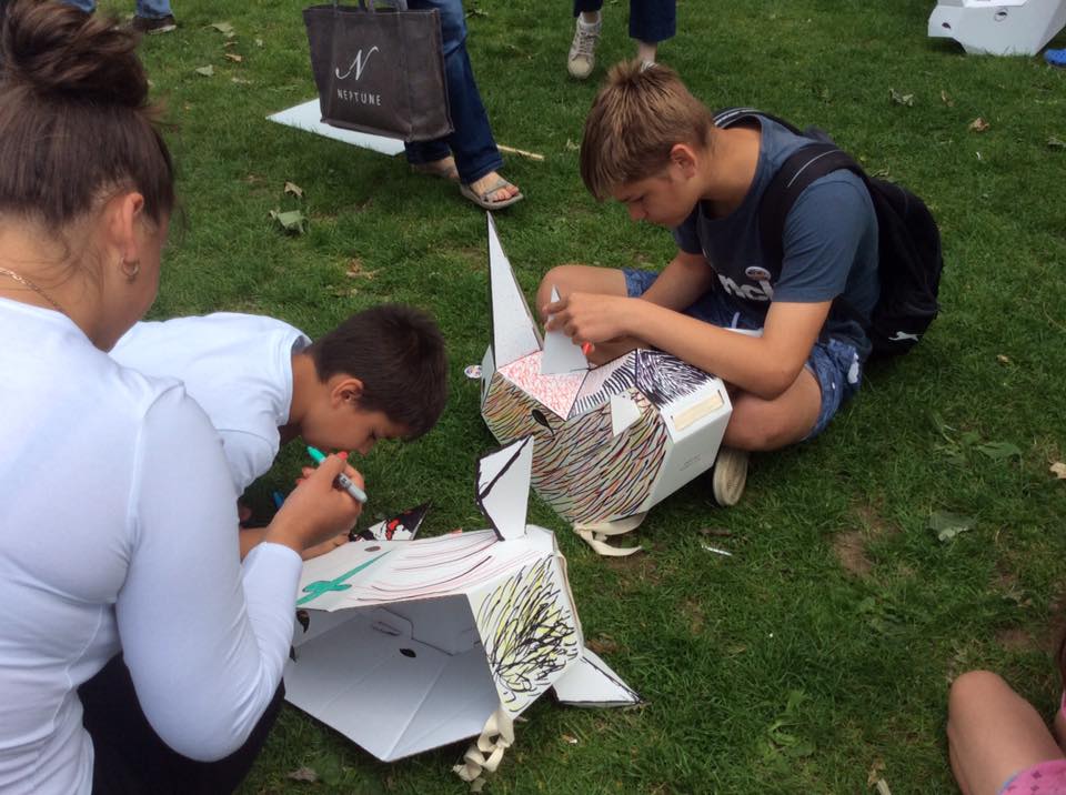 Two children sitting on the grass, decorating 3D card rhino masks.