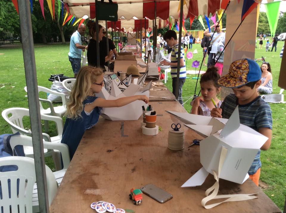 People (mostly children) at a long table, decorating 3D rhino masks with pen.