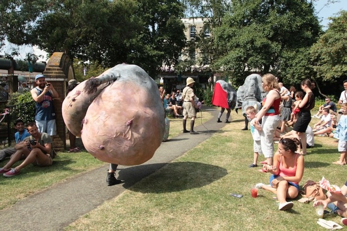 A giant rhino bum! Further away are two front-of-rhino puppets, all being worn by puppeteers. They walk down a path as people watch.